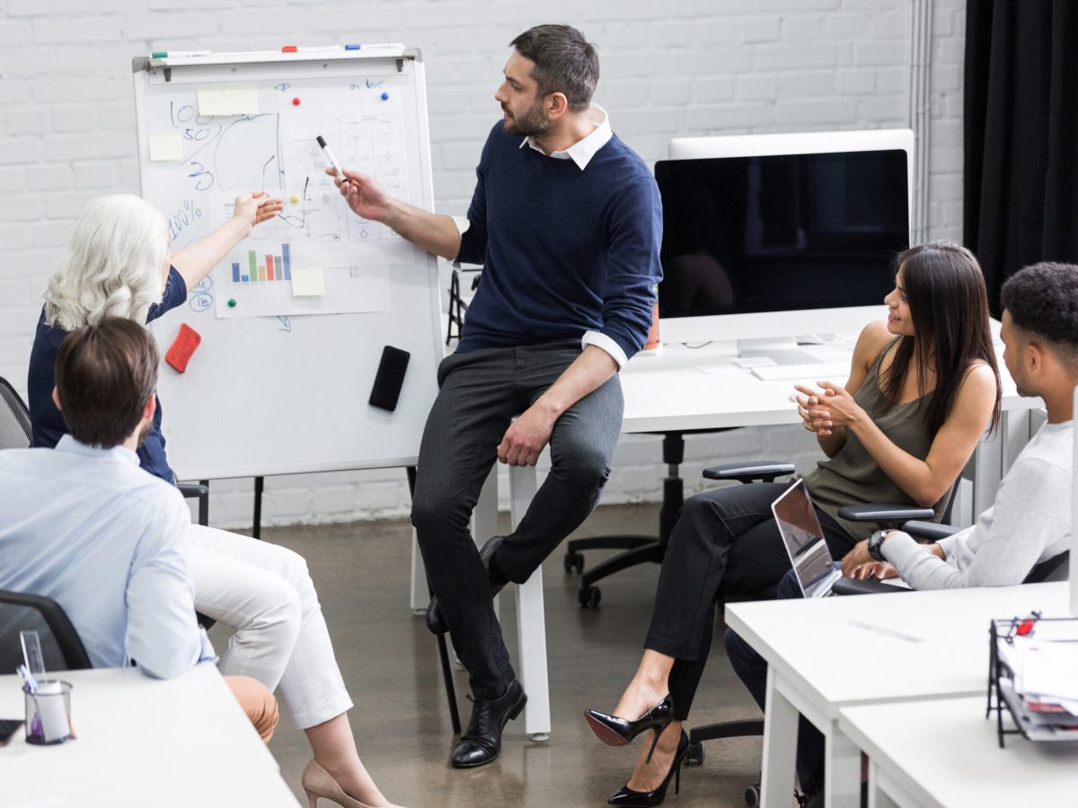 Creative people sitting at table in boardroom with man explaining business strategy